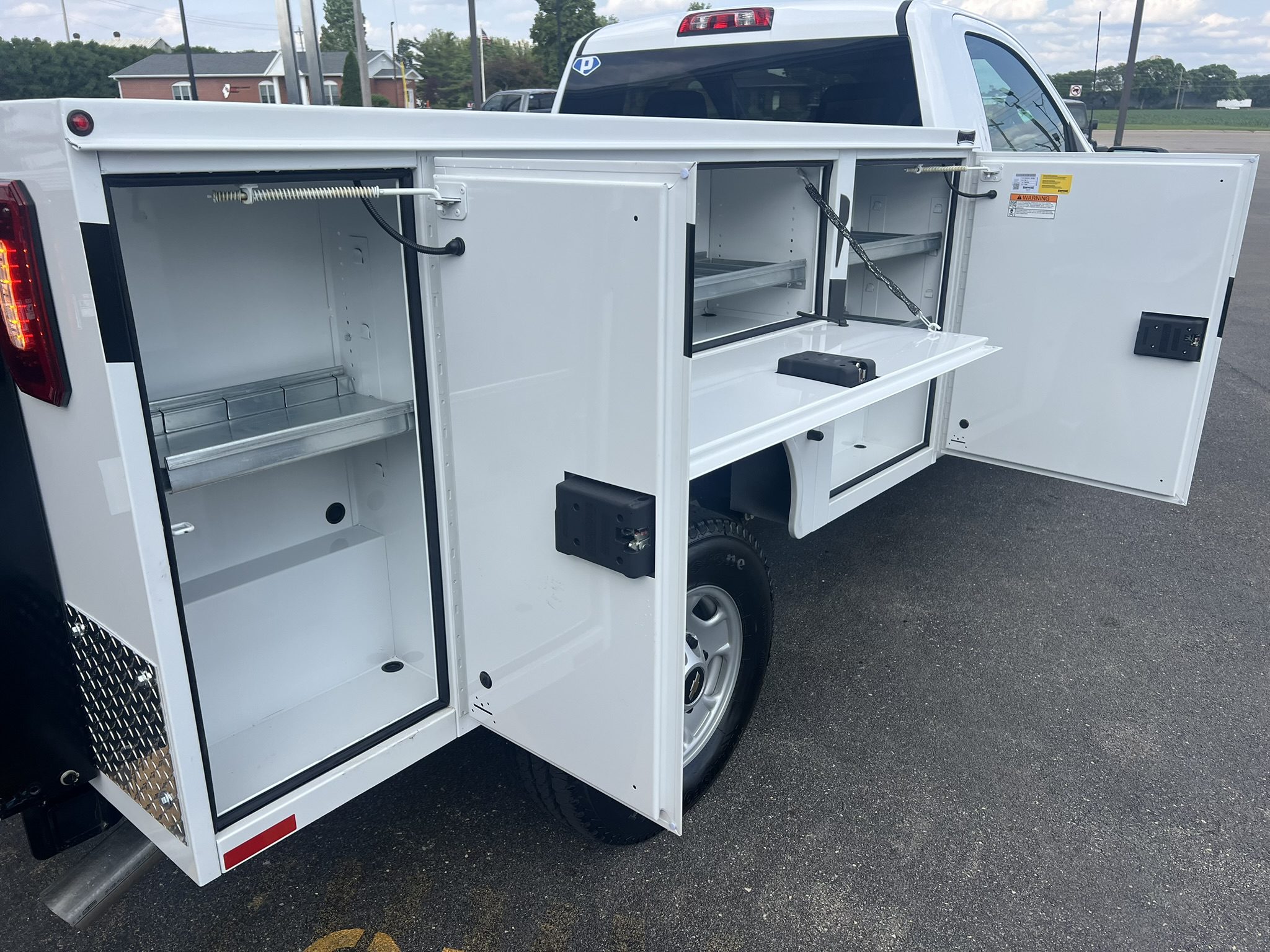 White utility truck with multiple open storage compartments and drawers.