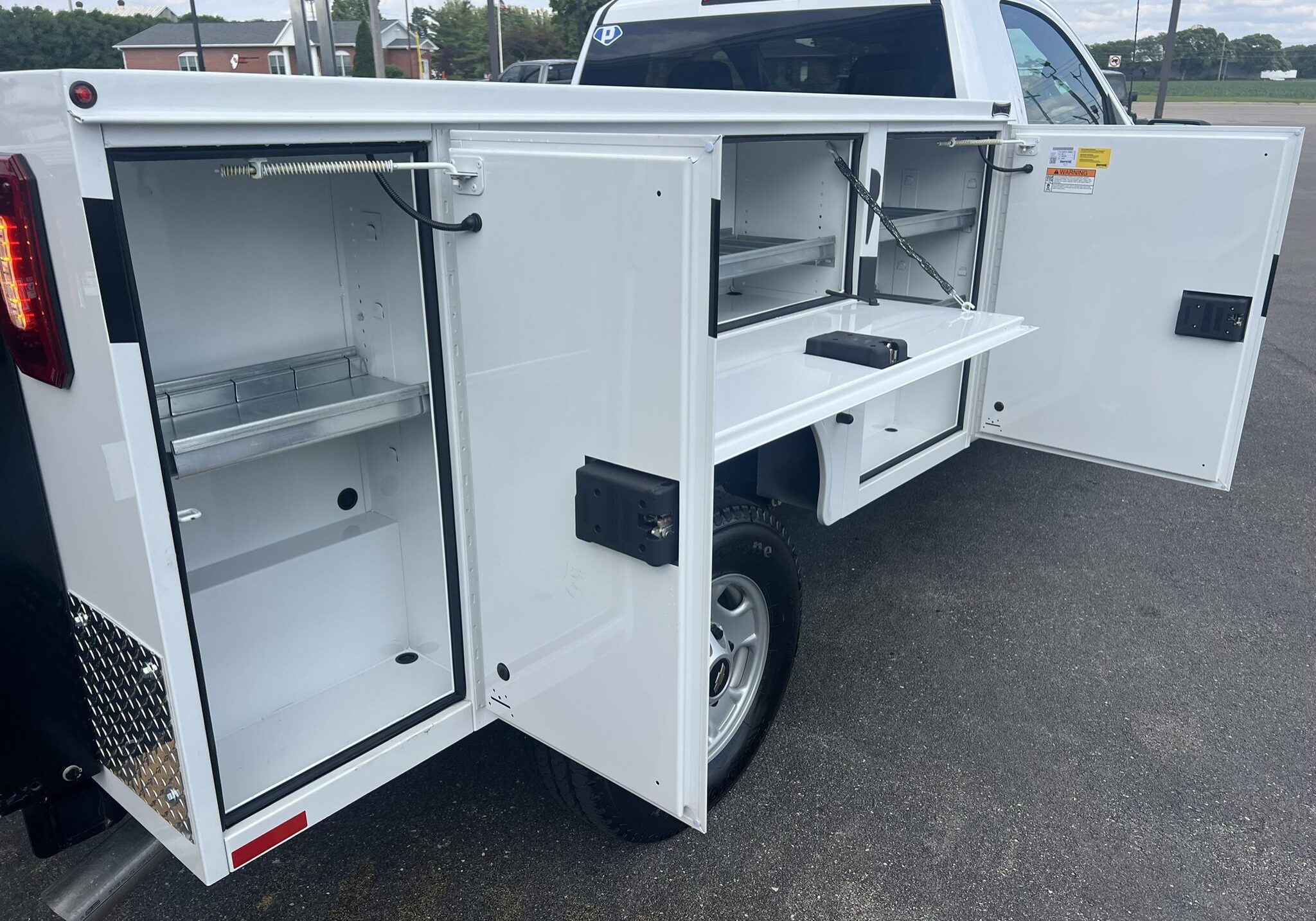 White utility truck with multiple open storage compartments and drawers.